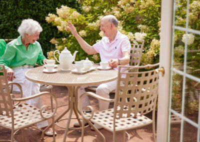 Two people laughing and enjoying tea outside next to flowers.