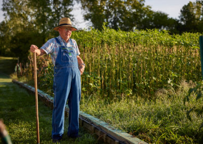 Man in overalls standing next to a large garden.