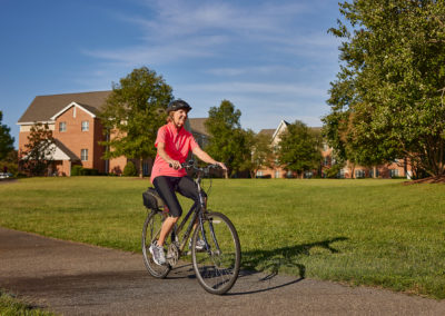 Woman riding a bike down a paved trail surrounded by a large greenspace.